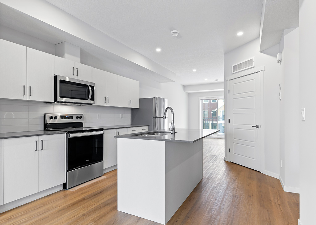 Kitchen with white cabinetry, dark countertop and stainless steel fridge, stove and microwave. Mid-tone, wood grain flooring throughout.